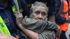 Rescue personnel carry an elderly person covered in mud after flash floods at Devghat in Nepal's Nuwakot district on 26 August 26 2026.