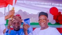 Aarẹ Bola Tinubu wọ asọ agbada toke tilẹ alawọ buluu ati filaalawọ waini, igbakeji rẹ, Kashim Shettima to wọ agbada funfun, fila dudu, duro tii lẹgbẹ, awọn mejeeji gbe asia ẹgbẹ oselu APC soke