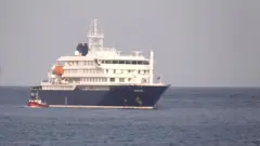 Um barco ao lado do navio de cruzeiro MV Hondius, atingido pelo hantavírus, ancorado no porto de Cabo Verde