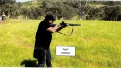 नवीद अक्रमच्या मोबाईल फोनवर सापडलेल्या व्हीडिओमधील स्क्रीनशॉट ज्यात त्याचे वडील बंदूक चालवण्याचं प्रशिक्षण घेत असल्याचं दिसत असल्याचं पोलिसांचं म्हणणं आहे