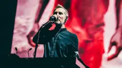 Роберт Дел Нажа, Massive Attack гуруҳи аъзоларидан бири, саҳнада клавишли чолғу олдида туриб микрофонга куйламоқда.