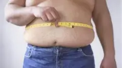 Қорни қанчалар каттарганини ўлчаётган семиз эркак