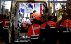 दुर्घटनामा परेका मानिसलाई एम्बुलेसमा राख्दै उद्धारकर्मीहरू