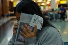 Mulher falando no celular, escondendo rosto com documentos