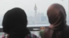 Dua wanita melihat tugu Monas yang tertutup oleh kabut polusi di Jakarta, Selasa (25/7/2023).