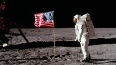 Sur l'image : une personne habillée d'une combinaison spatiale. L'astronaute est debout à côté du drapeau américain flottant