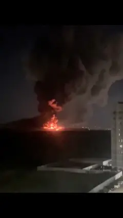 Жилой многоэтажный дом справа, а слева крупный горящий объект 