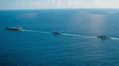 Um porta-aviões e dois navios atravessando um mar calmo