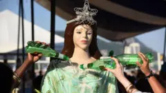 Representação de Iemanjá com pele branca, sendo molhada por garrafas