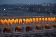 Iluminada ao anoitecer, a Ponte dos 33 Arcos, do início do século 17, na cidade de Isfahan atravessa o leito seco do rio Zayandeh Rud. Um grupo de pedestres é observado cruzando a ponte.