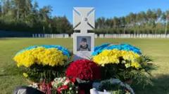 Могила на кладовищі, білий хрест із фото, біля могили живі квіти червоні та жовто-блакитні