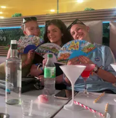 Tres mujeres jóvenes sentadas en un bar, sosteniendo abanicos de papel.