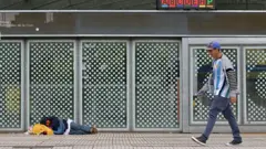 Homem passa em frente à estação de metrô Constitución, em Buenos Aires, enquanto uma pessoa dorme no chão.