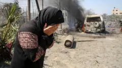 سيدة تغطي وجهها بكفيها وتظهر خلفها مركبة محترقة في منطقة مواصي غزة 