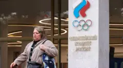 Женщина идет мимо колонны с надписью "Олимпийский комитет России"
