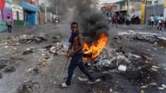 Um homem passa por um pneuboa esporte sga betchamas no Haiti