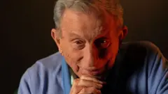 Haldun Dormen ellerini önünde kavuşturmuş, kameraya bakıyor.