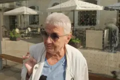 Жінка з коротким сивим волоссям в сонячних окулярах на зупинці громадського транспорту