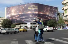 دو زن رهگذر در تهران برابر بیلبورد تبلیغاتی جنگ ایران و اسرائیل