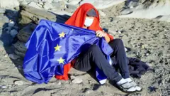 Migrante porta la bandera de la Unión Europea.
