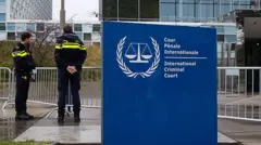 Dos hombres con chaquetas negras y amarillas se encuentran frente a la sede de la Corte Penal Internacional.