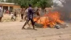 Ọ̀pọ̀ Aráàlú péjọ si ìdí iná tó ń jo, èyí tí wọn fi Taya mọto àti igi ko jọ, ọkùnrin kan ń da aloku taya sínú iná to ń jó náà èyí tí nnkan wa ninu rẹ 