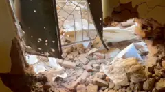 Tijolos e escombros espalhados no chão dentro de uma sala