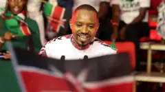 Boniface Mwangi yambaye ishati y'umweru n'amabara y'umukara n'umutuku, afashe ibendera rya Kenya