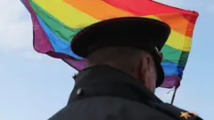 Um oficial russobaixar betano pcfrente a uma bandeira do movimento LGBTQIA+