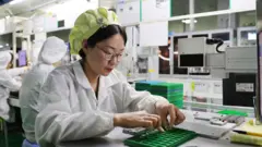 Una mujer ensambla manualmente piezas para teléfonos móviles en una fábrica