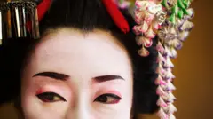 Uma foto de uma gueixa japonesa com maquiagem branca e delineador preto e vermelho. Ela usa um adereço de cabeça com flores e ornamentos