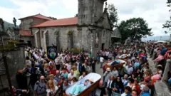 Pessoas levam caixões abertos aos ombros, em frente à igreja de São José de Ribarteme.