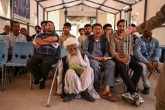 تصویر مهاجران افغان برگشته از ایران در نقطه مرزی میان دو کشور، یک مرد ریش‌سفید با لباس محلی افغانستان دیده می‌شود