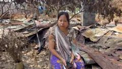 রামসু বাজারে পুড়ে যাওয়া টিনের ওপর বসে আছেন মুইখ্রাইপ্রু মারমা