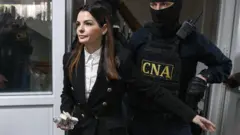 Евгения Гуцул в сопровождении мужчины в бронежилете входит в помещение в здании суда в Кишиневе.