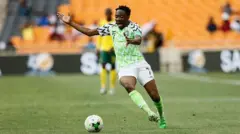 Ahmed Musa wear Nigeria 2018 Fifa World Cup jersey wey get lemon green, white and black design. E wear white shorts wey carry number 7 wit lemon green socks anf green boot.