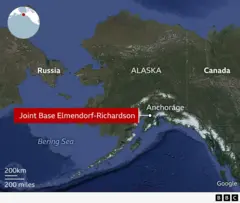 Un mapa muestra Alaska a la derecha, el estrecho de Bering en el centro y Rusia a la izquierda. La tierra en el mapa está en verde, mientras que el mar está en azul intenso. El mapa también incluye los nombres de los lugares representados: Rusia, Alaska, Canadá, Anchorage y la base conjunta Elmendorf-Richardson, así como el mar de Bering.