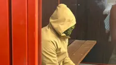 людина сидить боком у жовтому худі з закритим обличчям