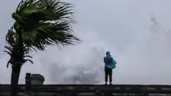 台灣基隆海旁一名身穿藍色雨衣的民眾在岸邊觀看巨浪滔天（11/7/2026）