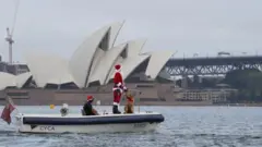 Father Christmas and his dog Rudolph arriving in Sydney Harbour to deliver gifts to the participants of the Rolex Sydney to Hobart yacht race which begins Boxing Day