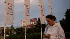 A woman holding a phone walks past white flags