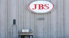 A fachada de um edifício da JBS, com o logotipo da empresa em destaque e uma placa indicando os escritórios da administração principal.