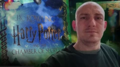 Egy szerkesztett kép, ami egy kopaszra nyírt hajú férfit mutat J.K. Rowling „Harry Potter és a Titkok Kamrája" című könyve előtt