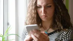 Uma mulher olha para o celular com expressão de contrariedade