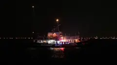 سفينة تابعة لأسطول الصمود العالمي تطفو في المياه بينما تقوم قوارب الحرس الوطني البحري التونسية بالتفتيش في ميناء سيدي بوسعيد، تونس