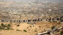 Longa fila de palestinos carregando sacos de farinha de caminhões de ajuda humanitária no norte da Faixa de Gaza, no dia 27 de julho de 2025