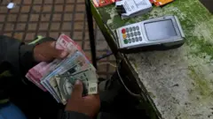 Un vendedor de lotería sostiene un fajo de billetes de distintos colores.