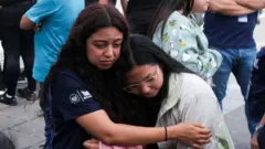 Dos mujeres se abrazan luego de evacuar su lugar de trabajo por un terremoto.