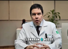 Imagem do médico Hélio Brasileiro de jaleco, falando com um microfone para uma câmera, em formato de vídeo de depoimento, com placa do Youtube ao lado