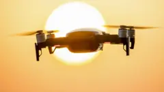 Un drone quadricoptère en vol stationnaire devant le soleil.